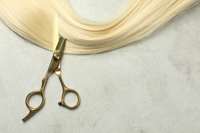 Photo of Professional hairdresser scissors with blonde hair strand on grey table, top view. Space for text