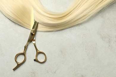 Professional hairdresser scissors with blonde hair strand on grey table, top view. Space for text