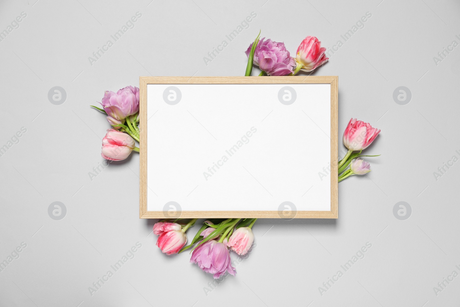 Photo of Empty photo frame and beautiful flowers on light gray background, top view. Space for design