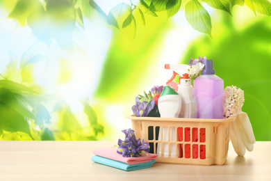 Image of Plastic basket with different detergents on wooden table, space for text. Spring cleaning concept 