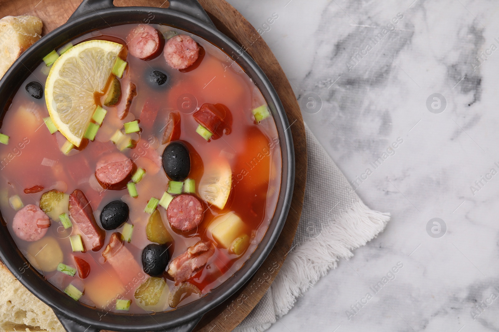 Photo of Meat solyanka soup with thin dry smoked sausages in bowl on white marble table, top view. Space for text