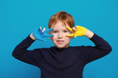 Photo of Little boy with hands painted in Ukrainian flag colors on light blue background. Love Ukraine concept