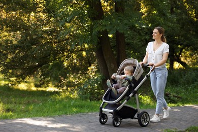 Photo of Happy nanny with baby in stroller walking in park, space for text