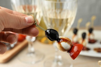 Woman holding tasty canape with black olive, mozzarella and cherry tomato on table, closeup