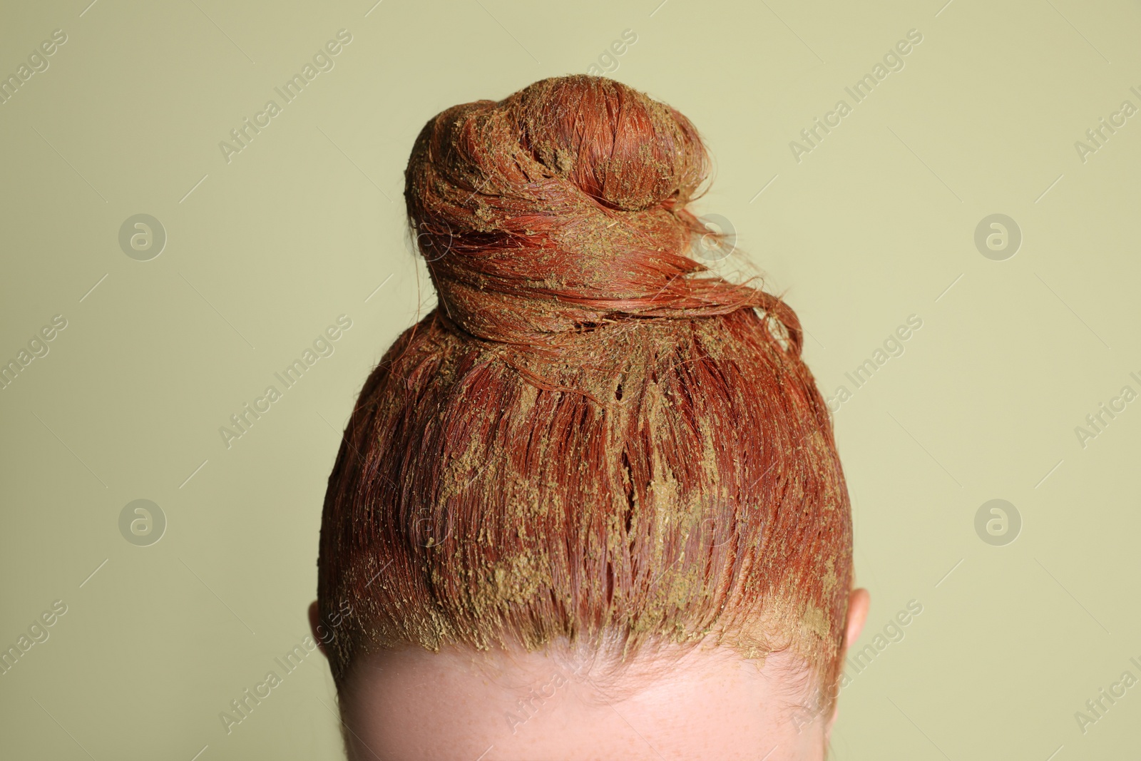 Photo of Young woman dyeing her hair with henna on light green background, closeup