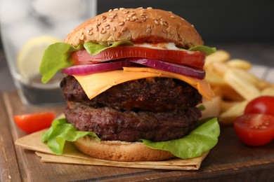 Tasty cheeseburger with patties, French fries and tomatoes on wooden board, closeup