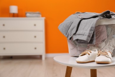 Laundry basket with baby clothes and shoes on white wooden table in child room, space for text