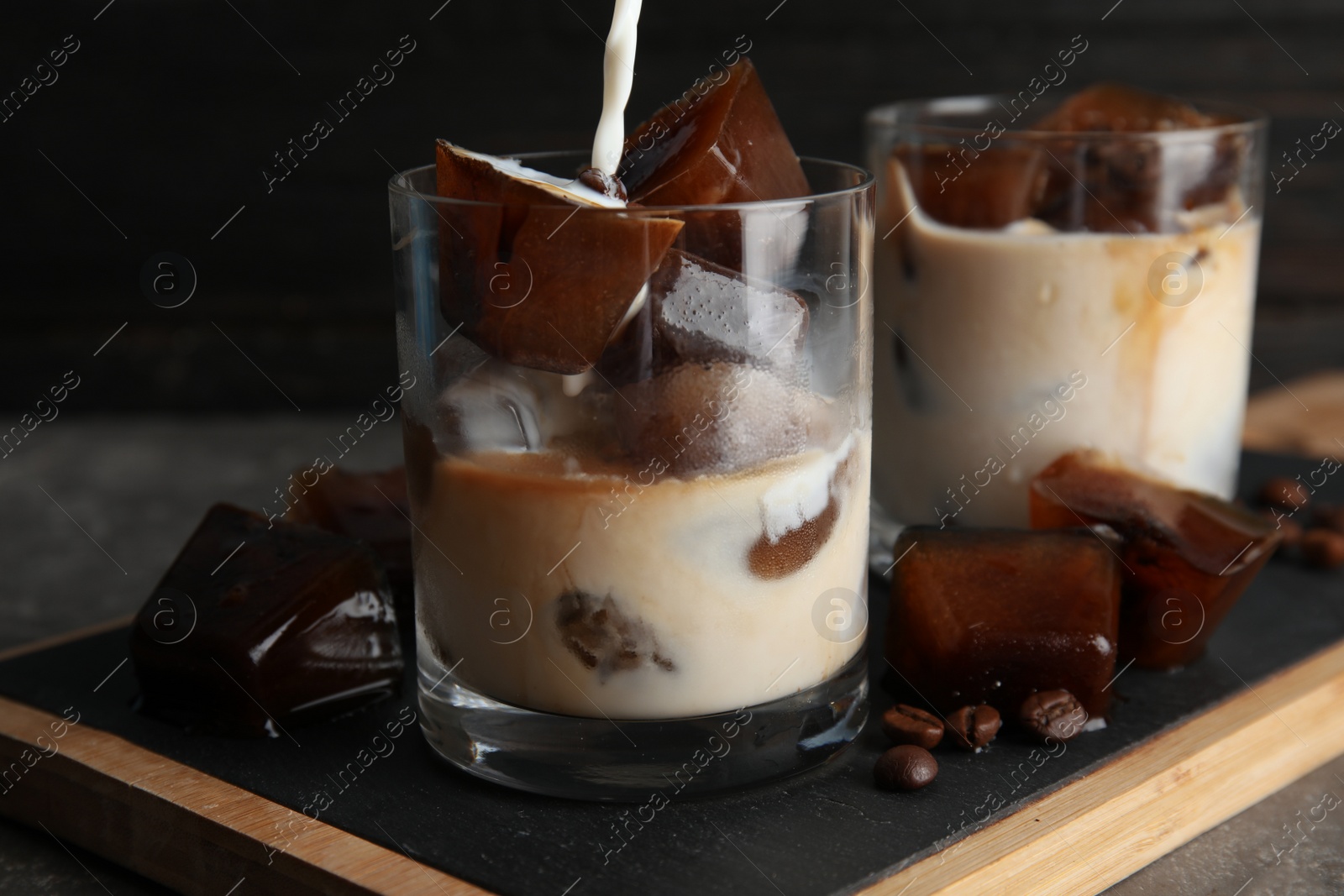 Photo of Pouring milk into glass with coffee ice cubes on table