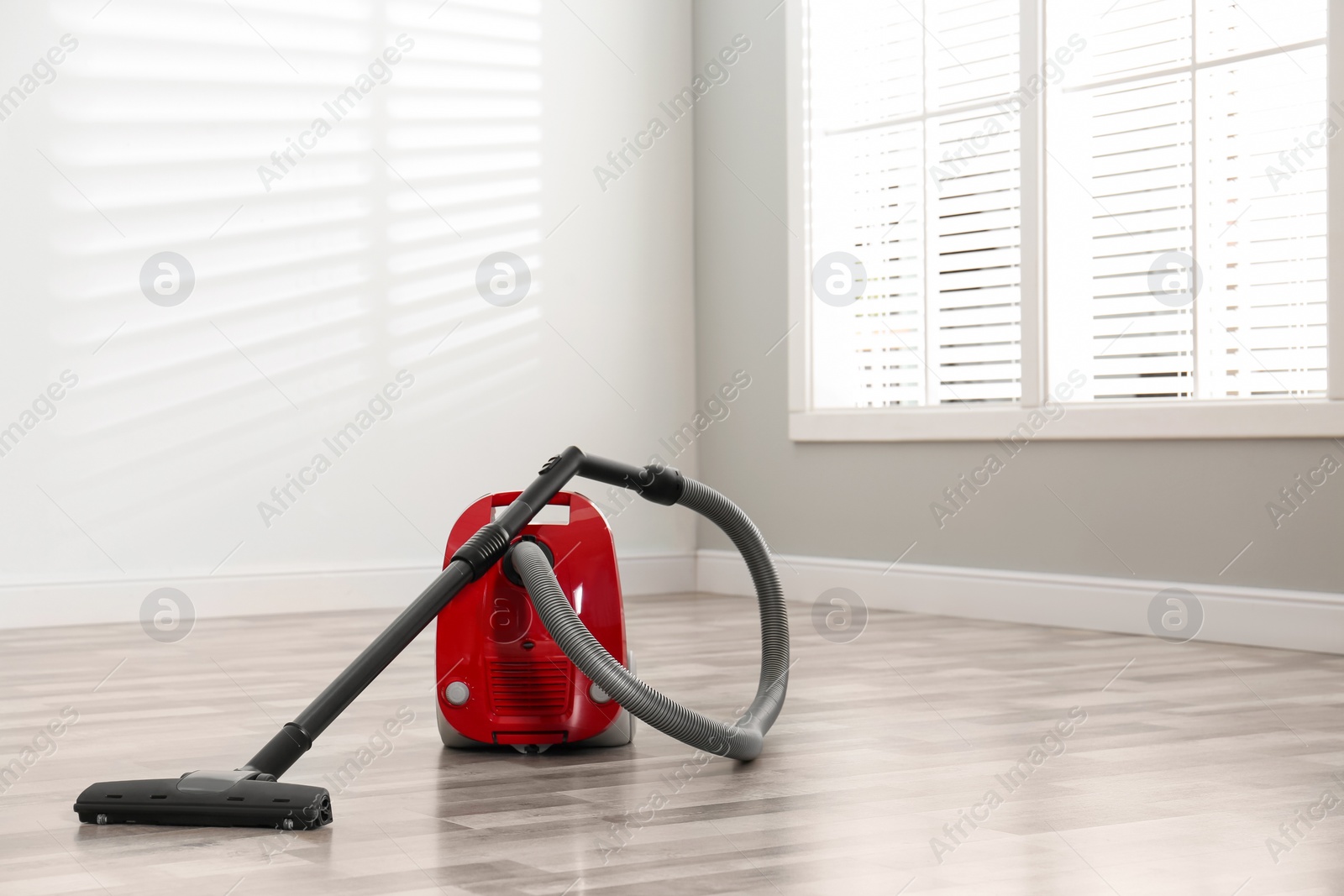 Photo of Modern red vacuum cleaner on floor indoors