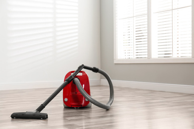 Modern red vacuum cleaner on floor indoors