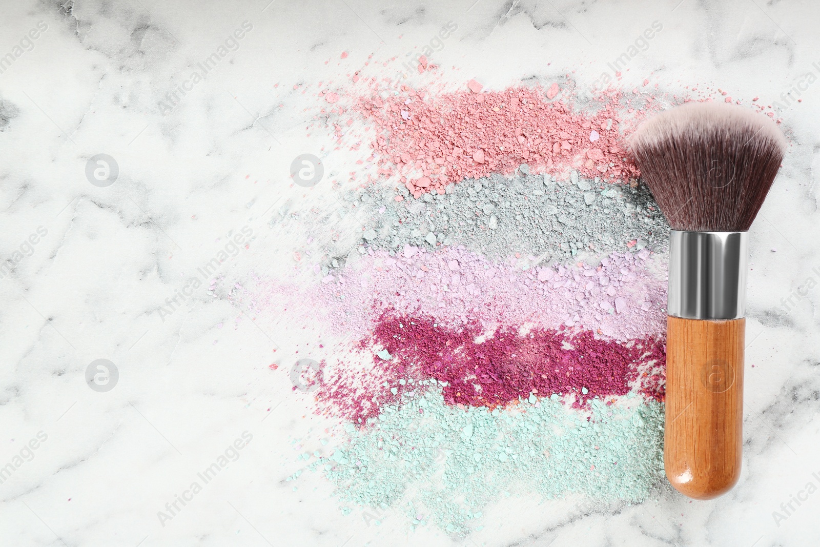 Photo of Makeup brush and scattered eye shadows on white marble table, flat lay. Space for text