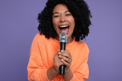 Beautiful woman with microphone singing on violet background