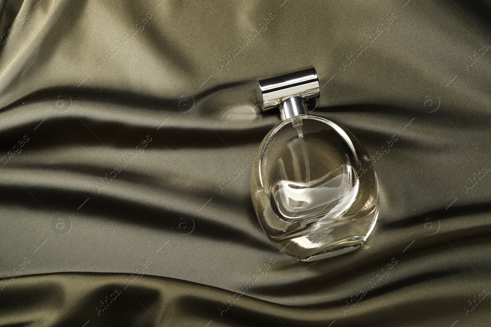 Photo of Luxury perfume in bottle on dark silk fabric, top view