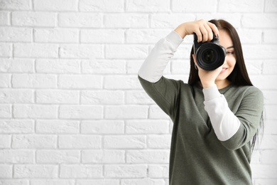 Female photographer with professional camera near brick wall