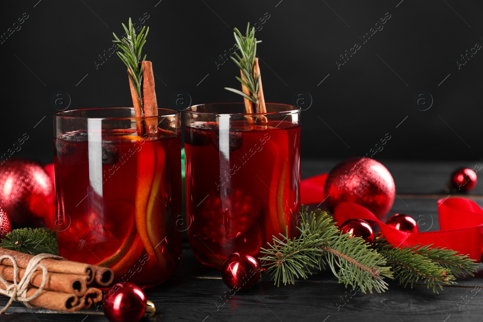 Photo of Aromatic Sangria drink in glasses, ingredients and Christmas decor on black wooden table