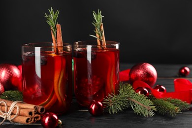 Photo of Aromatic Sangria drink in glasses, ingredients and Christmas decor on black wooden table