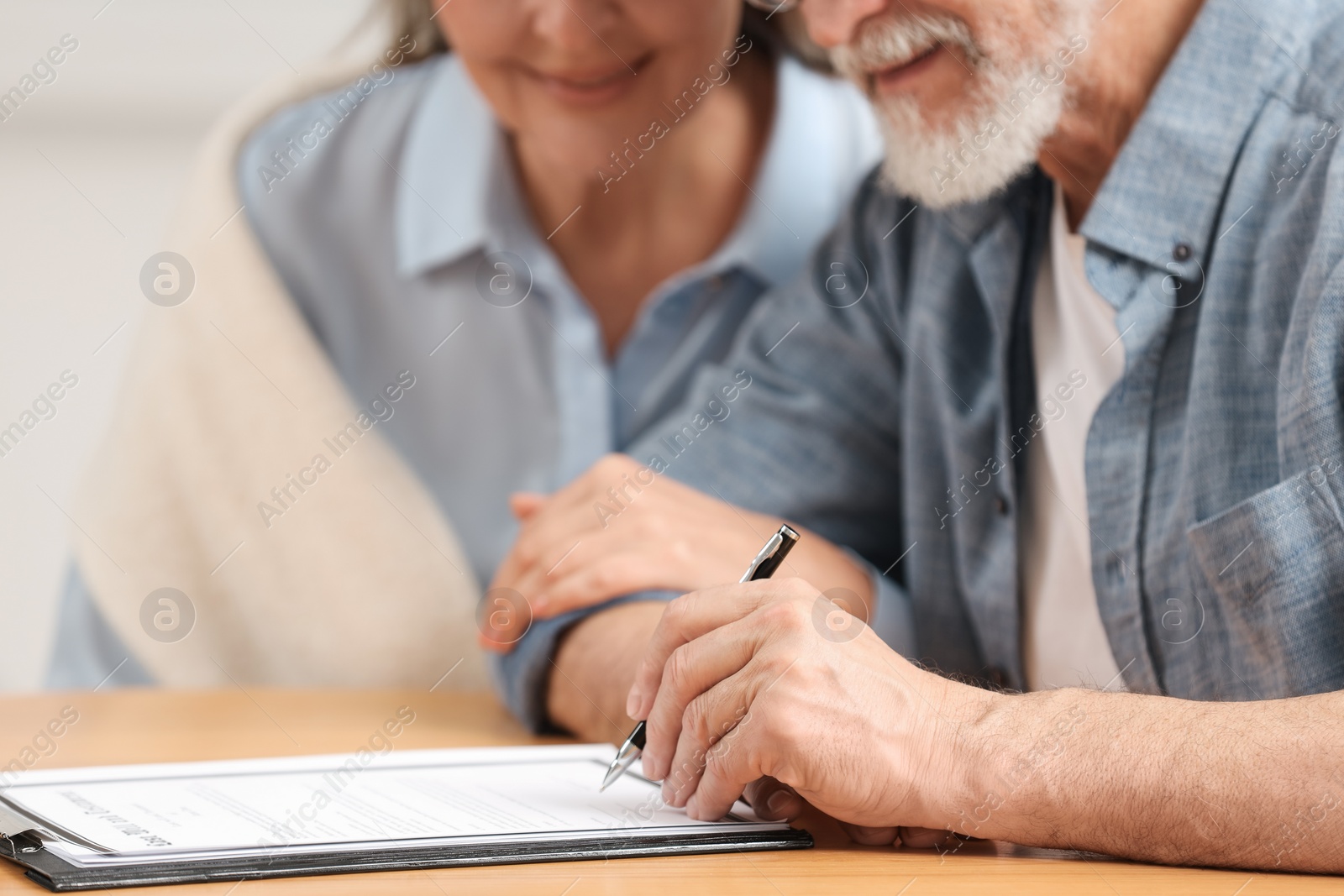 Photo of Senior couple signing Last Will and Testament indoors, closeup