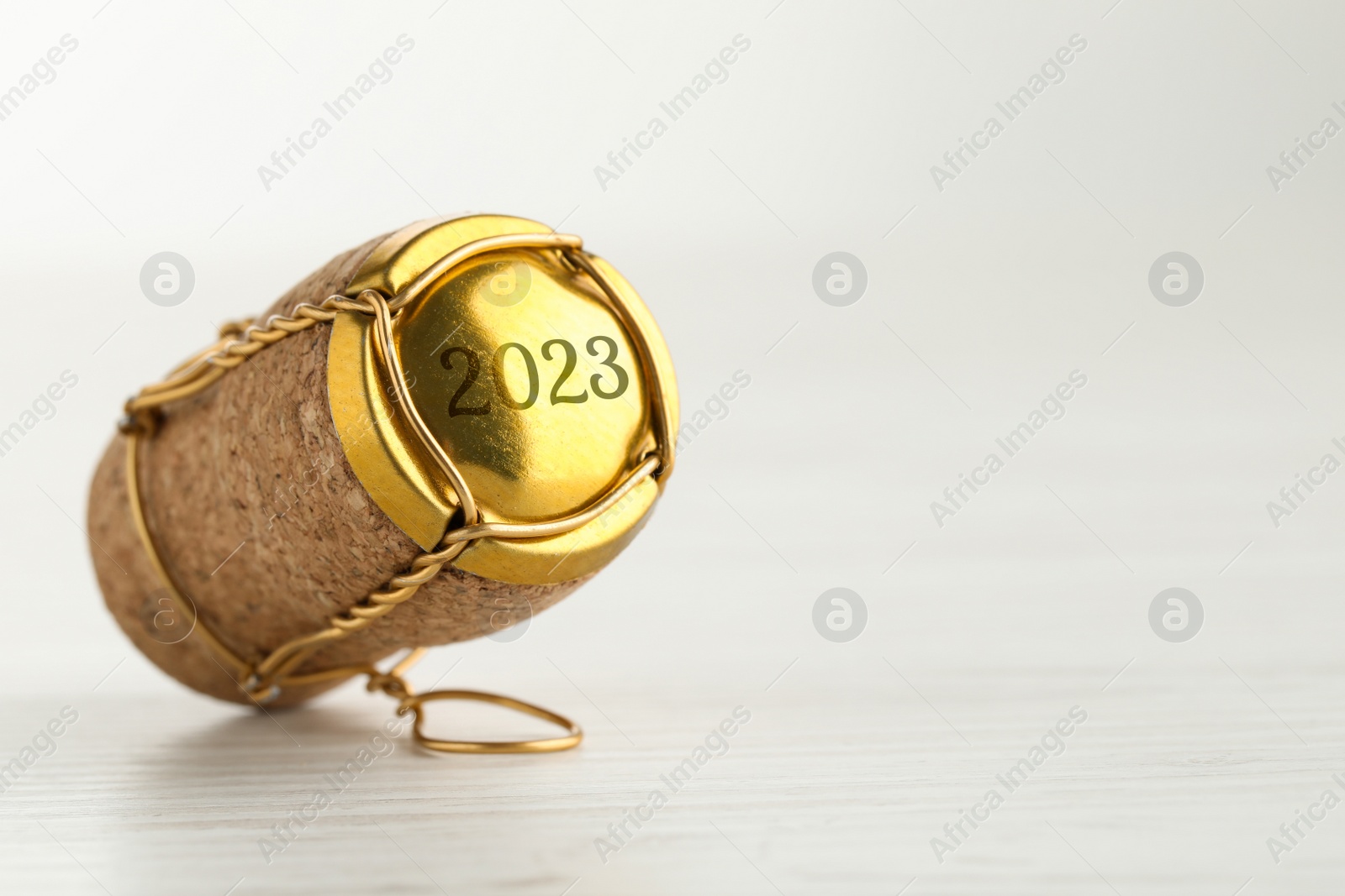 Image of Cork of sparkling wine and muselet cap with engraving 2023 on white wooden table, space for text. Space for text