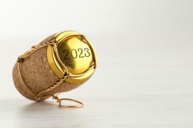 Image of Cork of sparkling wine and muselet cap with engraving 2023 on white wooden table, space for text. Space for text