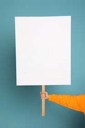 Woman holding blank sign on light blue background, closeup. Space for design