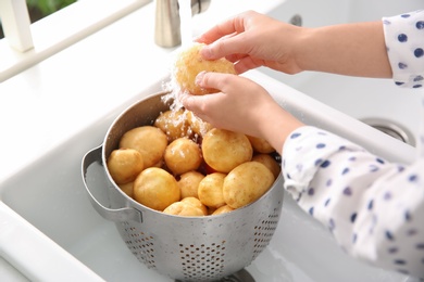 Photo of Woman washing fresh potatoes in kitchen sink, closeup