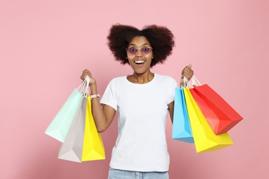 Photo of Happy African American woman in glasses with shopping bags on pink background