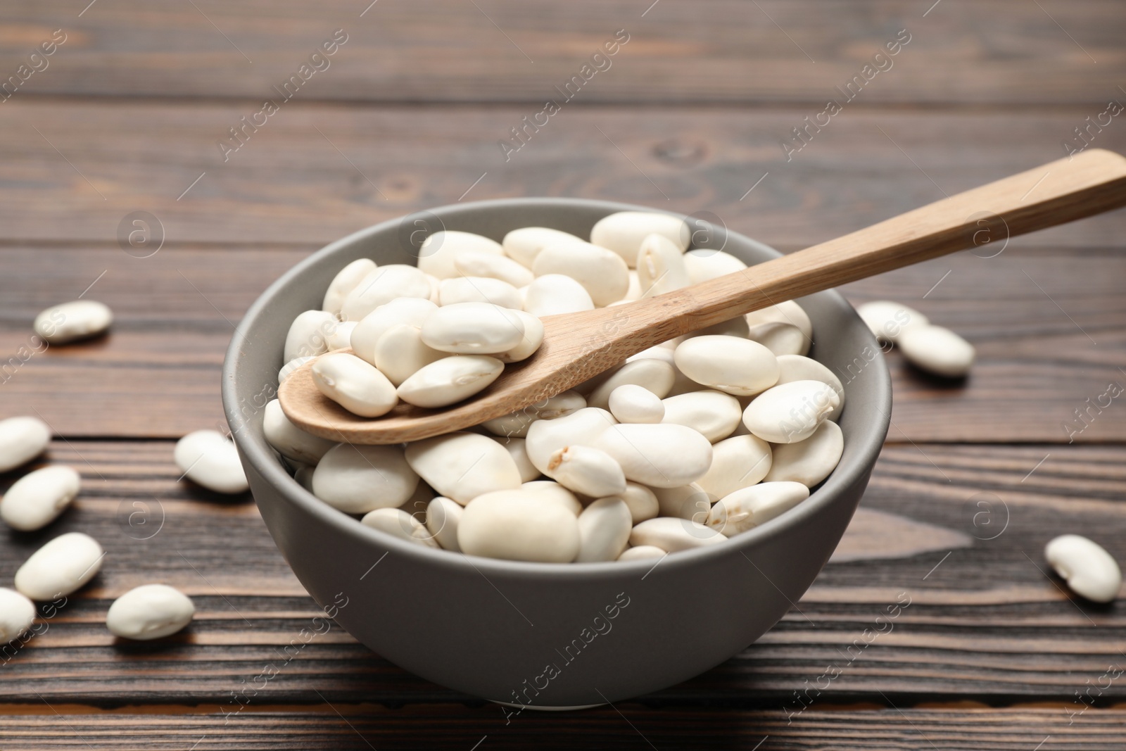 Photo of Raw white beans, bowl and spoon on wooden table, closeup