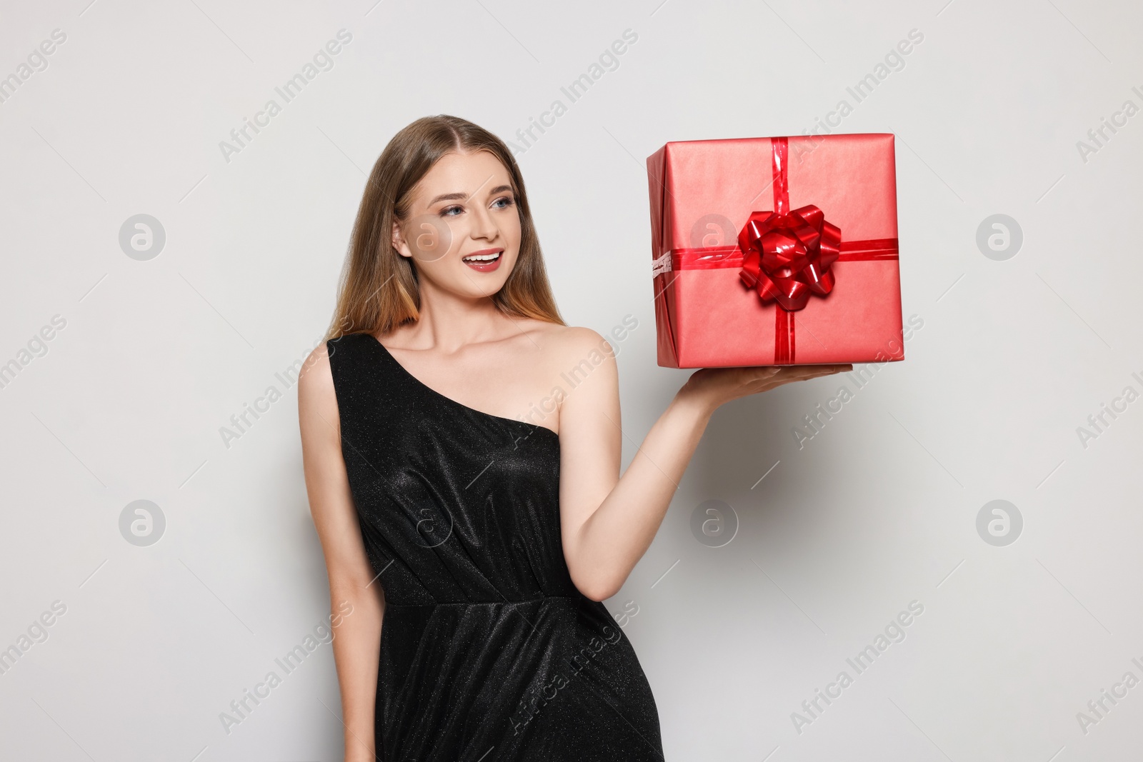 Photo of Portrait of beautiful young woman in elegant black dress with red gift box on white background