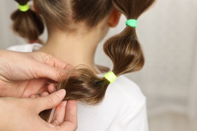 Photo of Professional stylist braiding girl's hair indoors, closeup