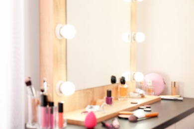 Photo of Blurred view of table with makeup products and mirror near white wall, closeup. Dressing room