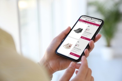 Woman shopping online via smartphone indoors, closeup