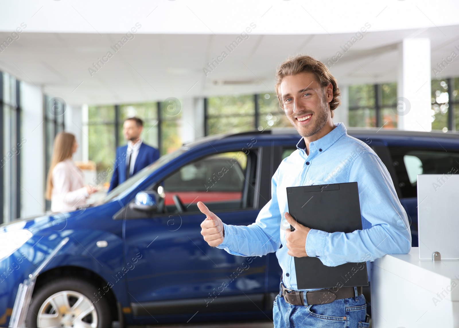 Photo of Salesman with clipboard near new car in modern auto dealership