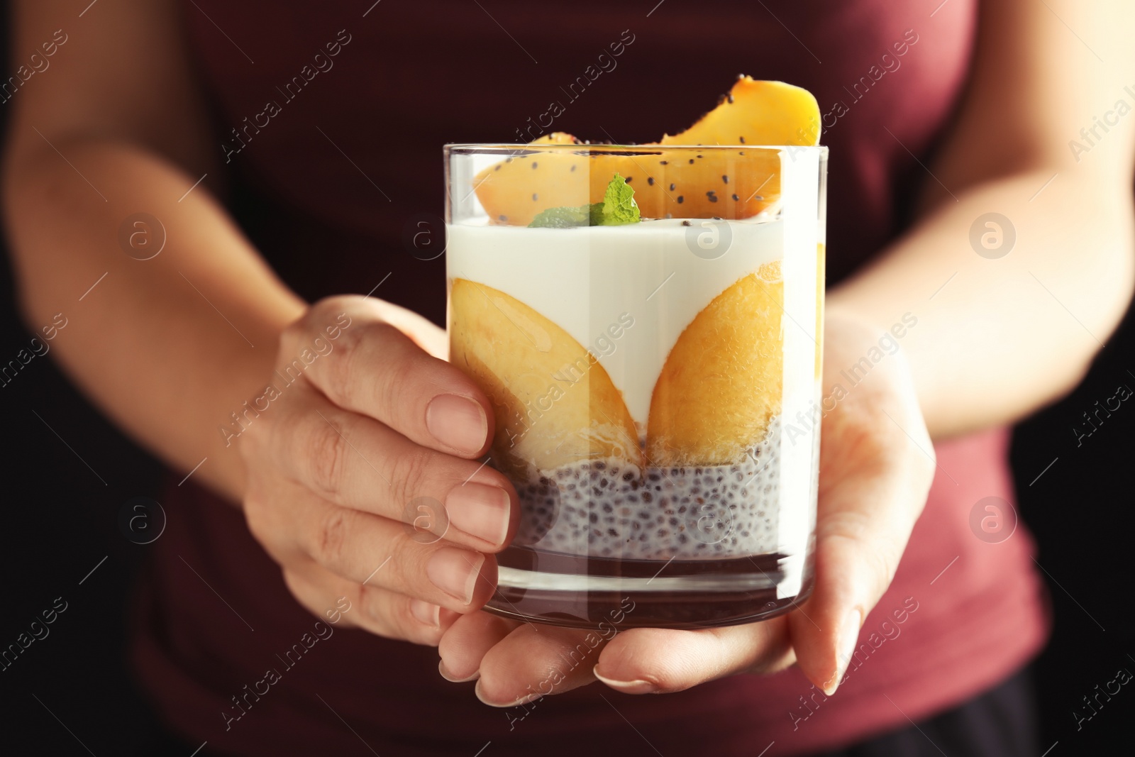 Photo of Woman holding tasty peach dessert with yogurt and chia seeds on black background, closeup