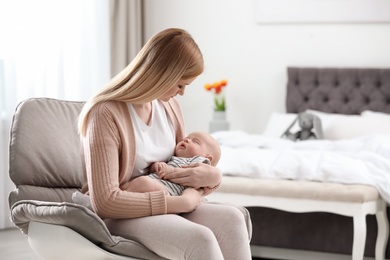 Mother with her little baby sitting in armchair at home