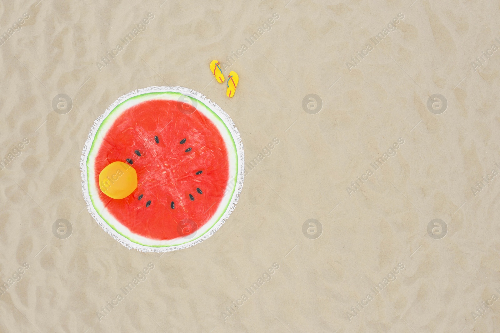 Image of Round watermelon beach towel, ball and flip flops on sand, aerial view. Space for text