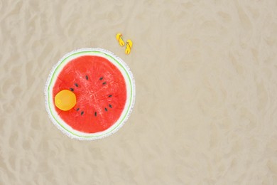 Round watermelon beach towel, ball and flip flops on sand, aerial view. Space for text