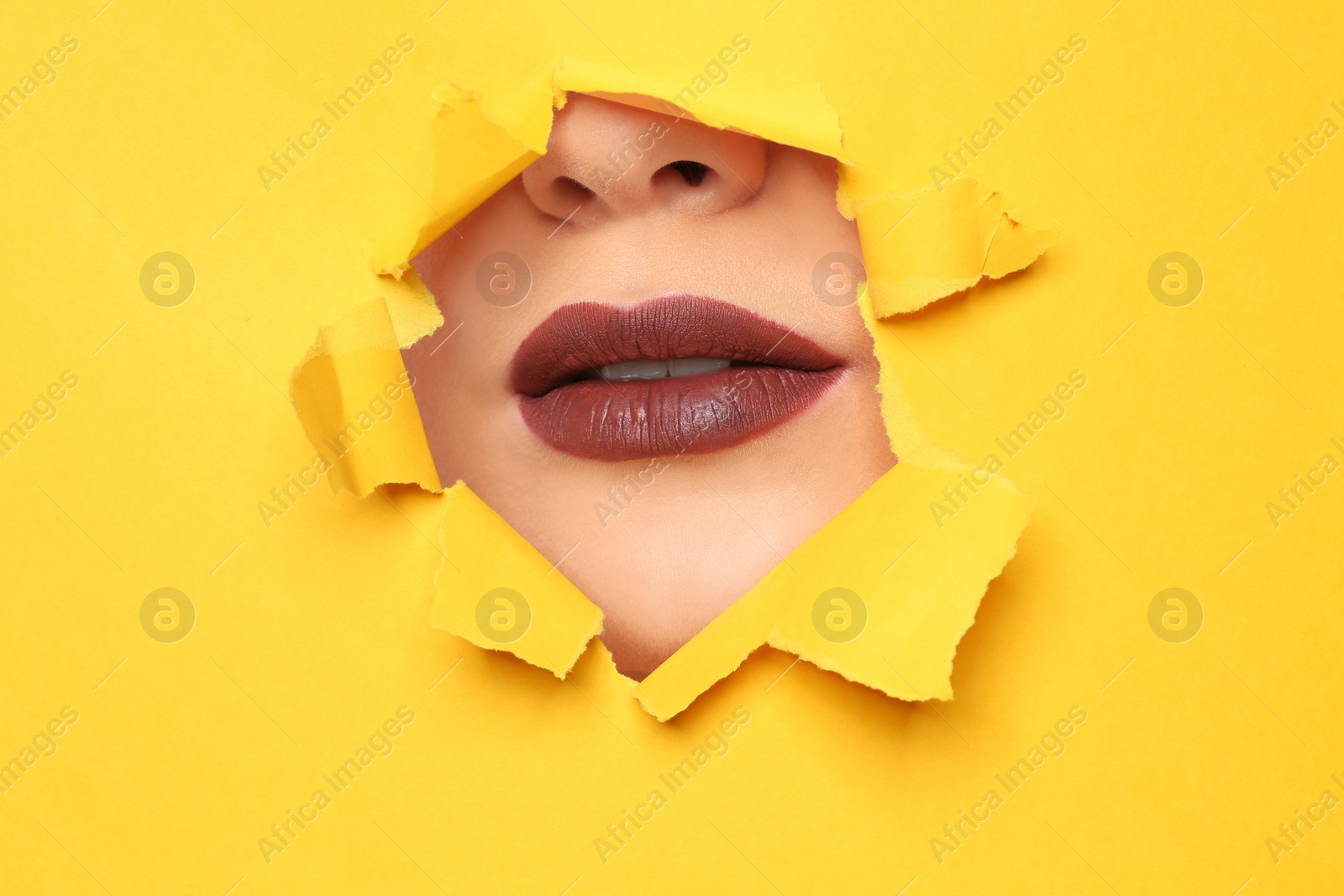 Photo of Lips of beautiful young woman with dark lipstick visible through hole in color paper