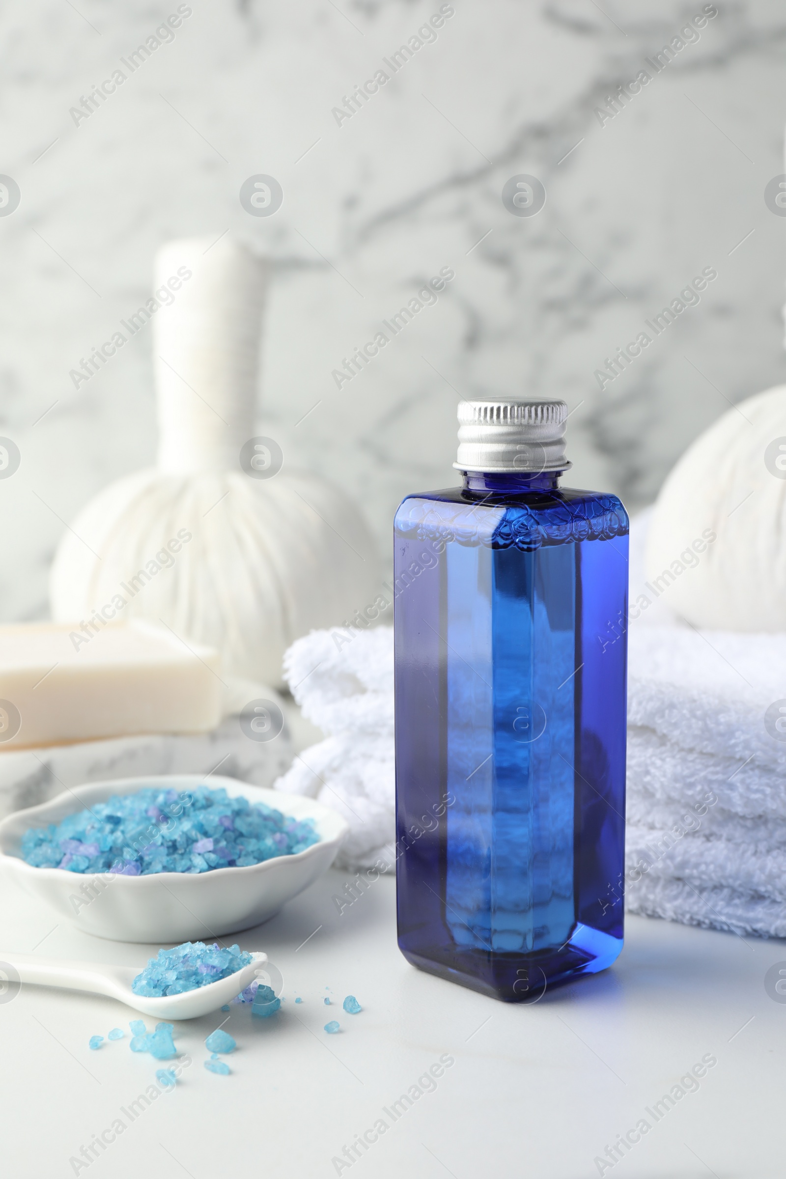 Photo of Spa composition. Bottle of cosmetic product, sea salt, towel, soap and herbal bag on white table