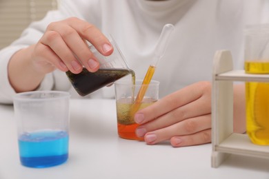 Photo of Girl mixing colorful liquids at white table indoors, closeup. Chemical experiment set for kids