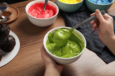 Photo of Woman mixing cream with green food coloring at wooden table, closeup