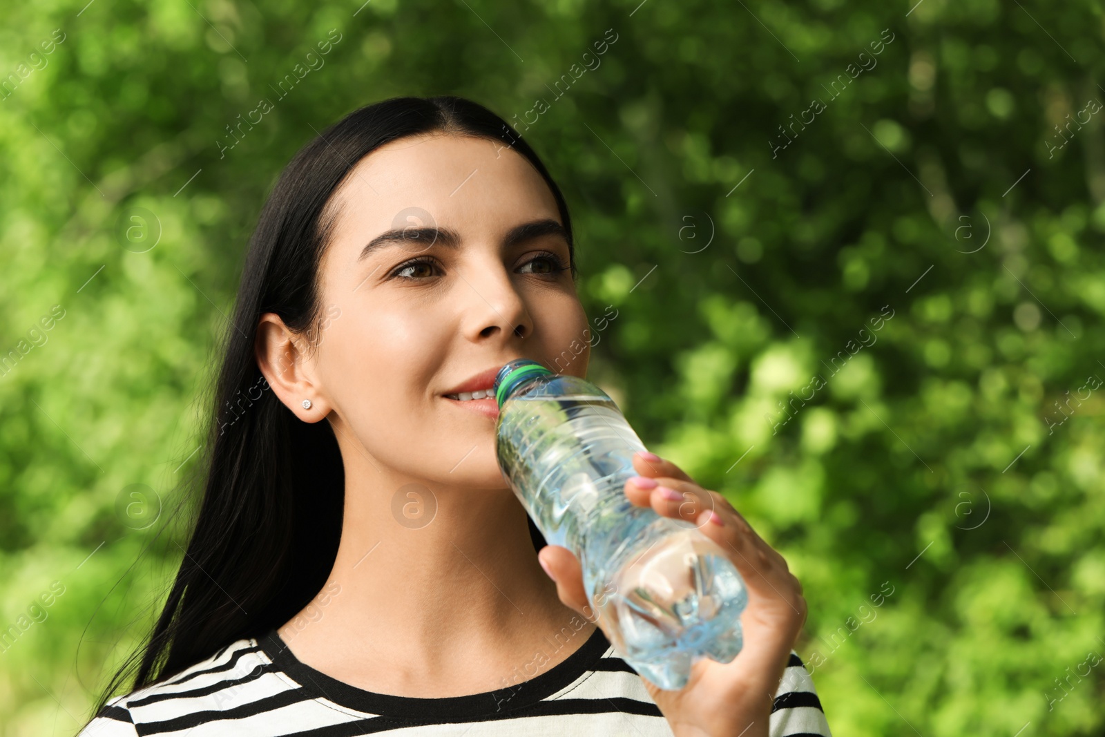 Photo of Young woman drinking water outdoors. Refreshing drink