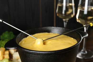 Photo of Dipping different products into fondue pot with melted cheese, closeup