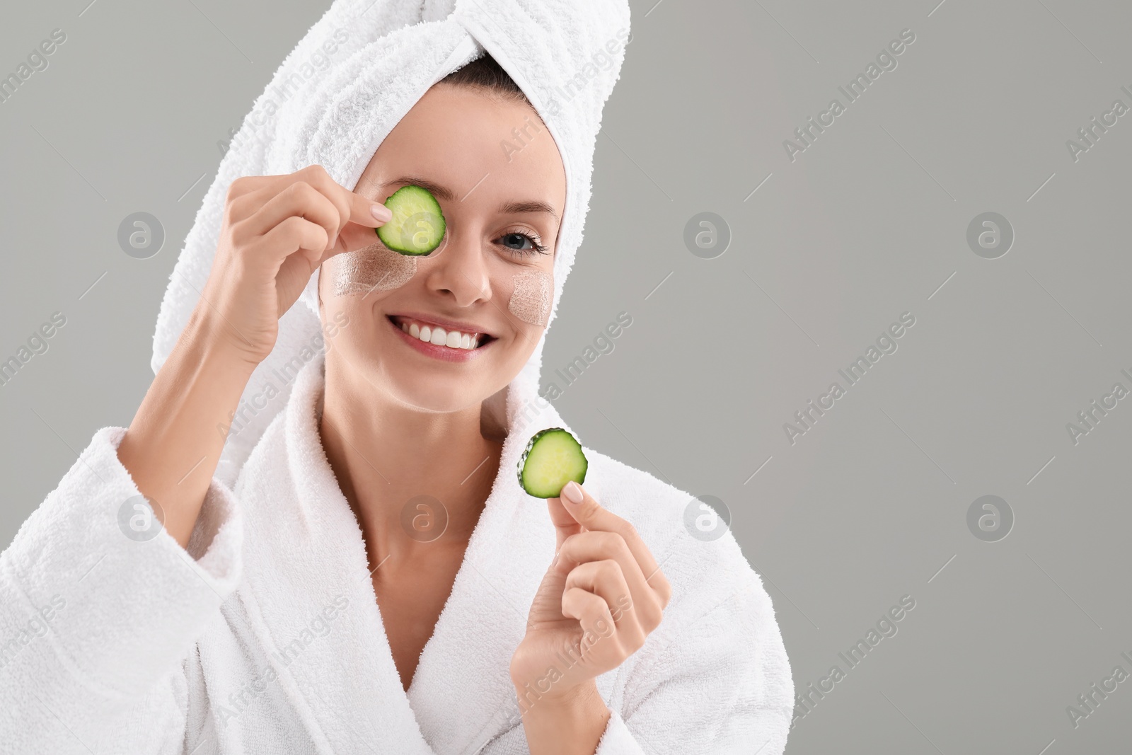 Photo of Woman with cosmetic product on her face and cucumber slices against grey background, space for text. Spa treatments
