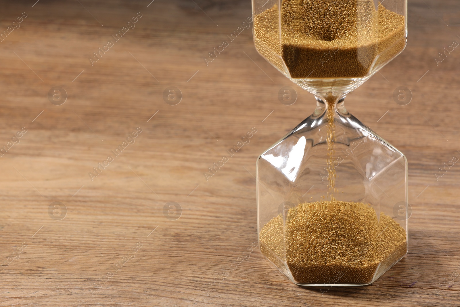 Photo of Hourglass with flowing sand on wooden table, closeup. Space for text