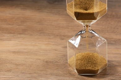 Photo of Hourglass with flowing sand on wooden table, closeup. Space for text