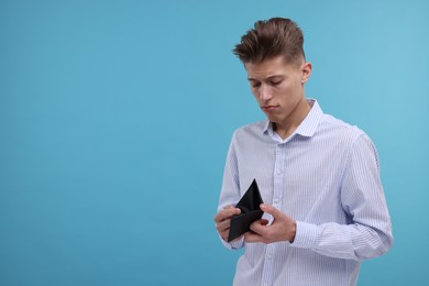 Photo of Upset man with empty wallet on light blue background. Space for text