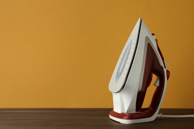 Photo of One modern iron on wooden table against orange background, space for text. Home appliance