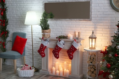 Photo of Stylish Christmas interior with decorative fireplace near white brick wall