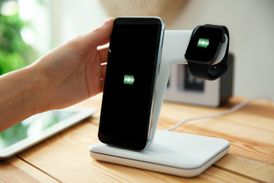 Photo of Woman putting mobile phone onto wireless charger at wooden table, closeup. Modern workplace accessory