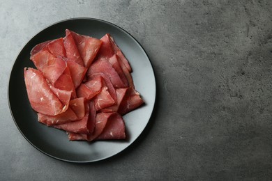 Photo of Plate with tasty bresaola on grey table, top view. Space for text